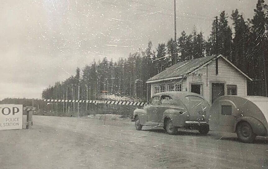 A car and a small trailer heading into Canada. highway in those early days